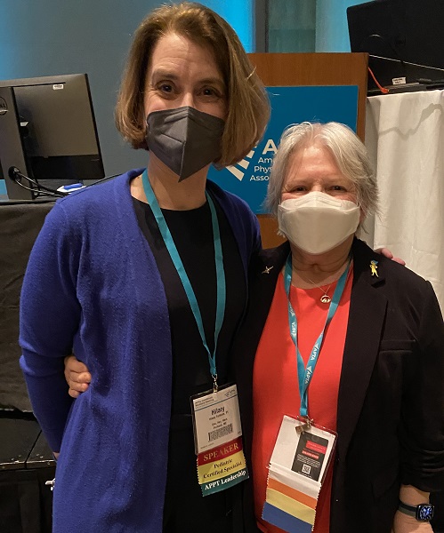 One tall and one shorter white women wearing surgical masks and event lanyards.